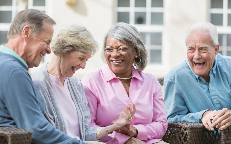 A group of cheerful senior friends smiling and laughing while enjoying each others company outdoors.