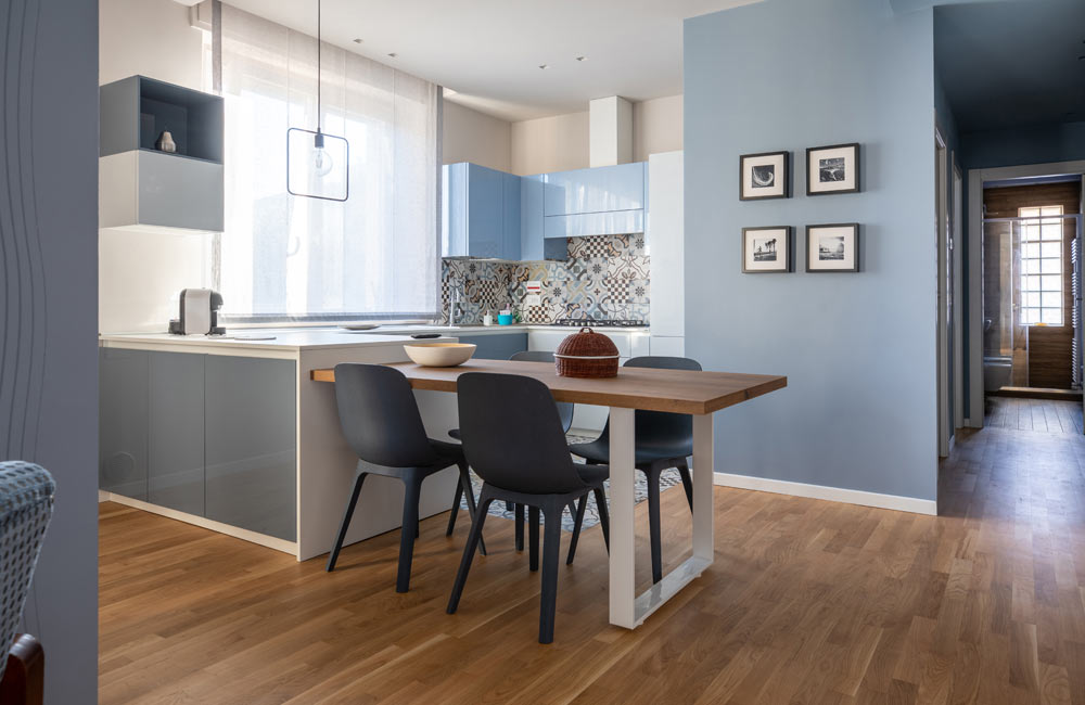 Modern kitchen and dining area with wooden flooring, blue cabinets, and wall art.