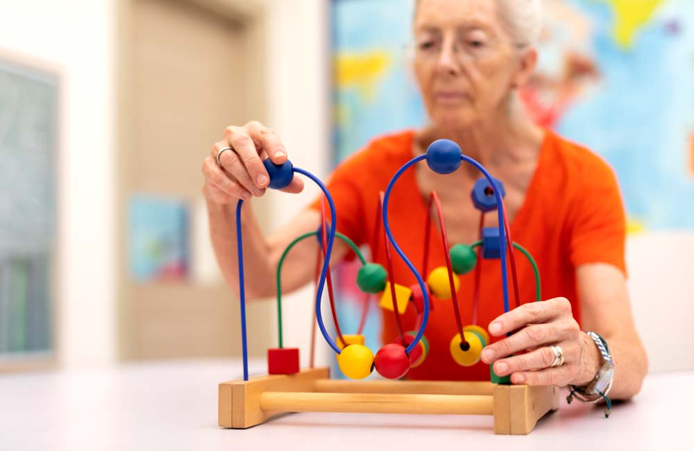 Elderly woman engaging in memory care activity at a senior center with colorful bead maze toy.