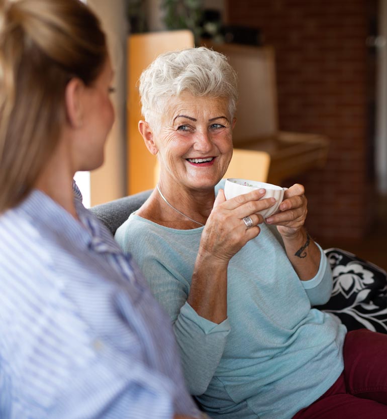 Smiling senior woman holding a cup, enjoying a conversation with a team member