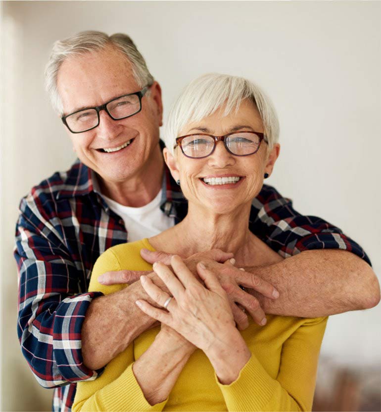 Senior couple wearing glasses, embracing and smiling joyfully while posing indoors.